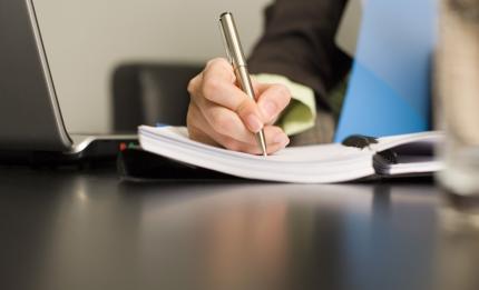 a hand holding a pen and writing in a note book