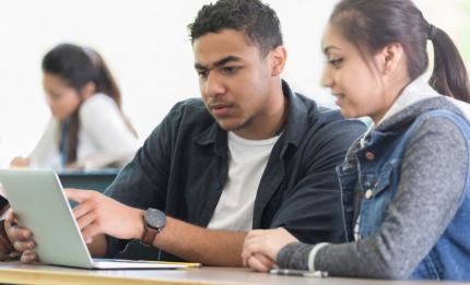 Two students discussing something on a laptop screen