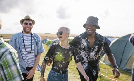 Three happy friends walk between tents at a music festival