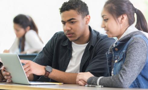 Two students discussing something on a laptop screen