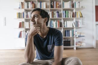 A man sitting in front of a bookshelf, looking up and smiling