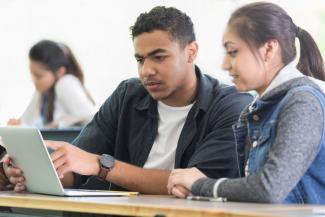 Two students discussing something on a laptop screen