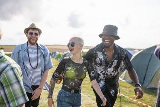 Three happy friends walk between tents at a music festival